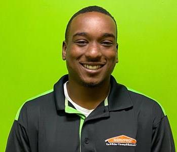 Male employee with black shirt smiling in front of a green background