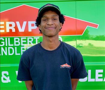 Male employee with SERVPRO hat smiling in front of a green background